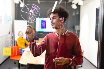 Young biracial male app developer drawing chart on glass in board room