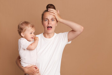 indoor shot of young tired shocked mother holding a child in her arms, female wearing white casual s