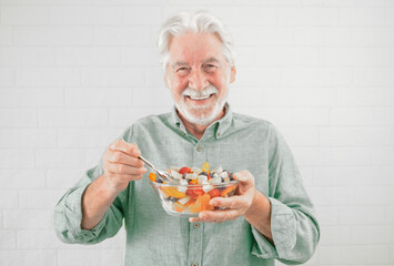 Wall Mural - Happy caucasian senior man holding a glass bowl with fresh summer fruit salad, ready to eat