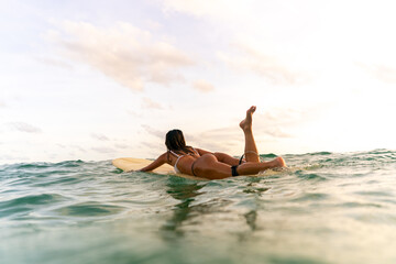 Asian woman surfer paddling surfboard and riding the wave in the sea at tropical beach at summer sunset. Healthy female enjoy outdoor activity lifestyle water sport exercise surfing on travel vacation