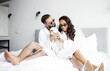 © Yuliia - Luxury newlyweds dressed in bathrobes playing with a dog in bed.
