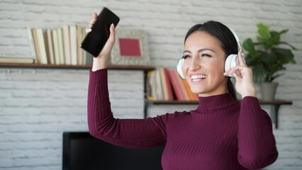 Wall Mural - Video of pretty young woman listening to music with mobile phone while dancing in the living room at home.