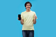 © IndiaPix - Portrait of a teenage boy holding a Smartphone and gesturing while standing against blue background