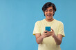 © IndiaPix - Portrait of a happy teenage boy using Smartphone while standing against blue background