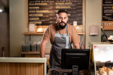 Male barista at counter using cashbox computer in cafe store. Indian Waiter in apron working in coffee shop.small business, people and service