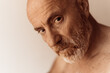 Bald man with bare torso and unkempt beard looks with serious expression, close-up and unfocused background