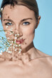 © Peakstock - Beauty portrait of caucasian young woman with healthy moisturized facial skin and blue eyes with flowers. Skin care concept