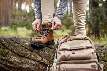 Wall Mural - woman tying shoelace on her hiking boot. tourist is getting ready for hike at forest trekking trail