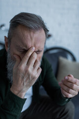 Wall Mural - senior man with beard covering face while suffering from headache.