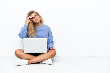 Wall Mural - Girl with curly hair with a laptop sitting on the floor having doubts and with confuse face expression