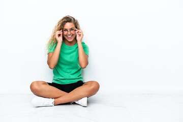 Wall Mural - Girl with curly hair sitting on the floor with glasses and surprised