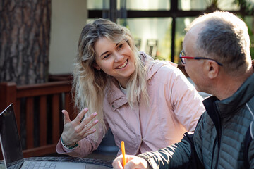 Portrait of young joyful woman daughter trainer talking to middle-aged man father, explaining information with laptop.