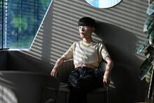 Portrait of Asian slim male,cross-dresser with crop-top shirt looking out of window with sad eyes and faded sunlight. Homosexuality modeling concept.