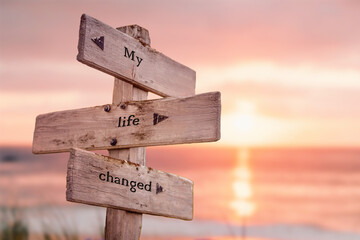 my life changed text quote on wooden crossroad signpost outdoors on beach with pink pastel sunset colors. Romantic theme.