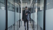 Man In Business Suit Walking In Empty Office Corridor, Looking At Watch Before Meeting