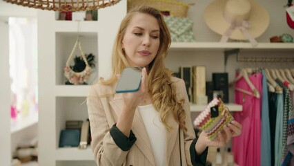 Poster - Young blonde woman shop assistant talking on the smartphone holding purse at clothing store