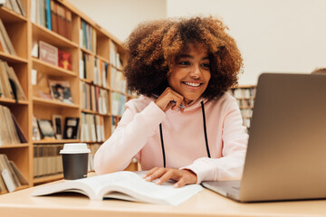 Wall Mural - Smiling girl with curly hair looking at laptop and preparing exams