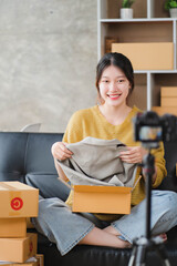 Young Asian women blogger showing clothes in front of the camera to recording vlog video live streaming at her shop. Network technology Business online influencer on social media concept