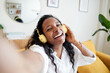 © CarlosBarquero - Happy selfie of cheerful young woman listening to music with headphones on soft couch at home in day off.