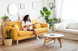 © CarlosBarquero - Woman playing Ukelele on living room sofa at home. Guitar music lessons indoors. Beautiful Latin girl comfortable at home enjoying cheerful music. Concept of leisure and relaxation.