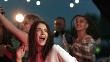 Portrait happy brunette curly woman dancing at night clubbing roof party with people friends crowd