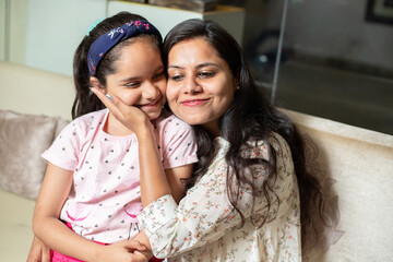 happy playful indian mother hug her daughter sitting together at home, love and care, asian woman wi