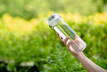 Hand Holding A Clean Drinking Water Bottle. Plastic Bottle Of Drinking Water With Green Blurred Background. 