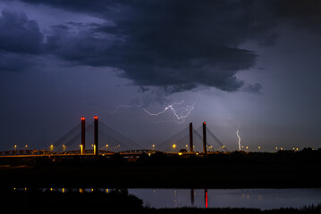 Wall Mural - dramatic night time image of lightning strikes near a cable-stayed bridge over a river