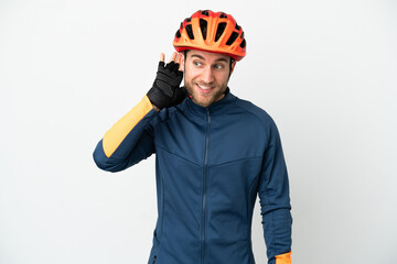 Wall Mural - Young cyclist man isolated on white background listening to something by putting hand on the ear