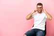 © luismolinero - Young man sitting on a chair over isolated pink background frustrated and covering ears