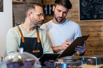 Couple owners bakery working while analyzing report for order delivery with digital tablet in a healthy pastry shop.