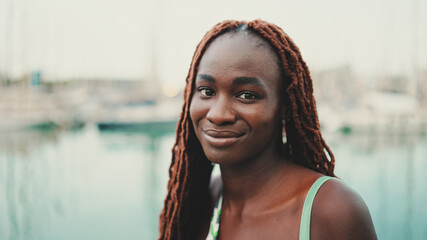 Wall Mural - Woman with African braids wearing top looks at the yachts and ships standing on the pier in the port.