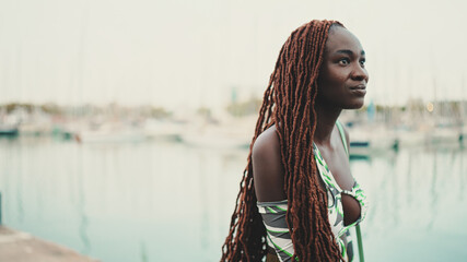 Wall Mural - Woman with African braids wearing top looks at the yachts and ships standing on the pier in the port.