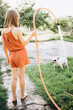 © Анна Молько - a girl in an orange overall plays with a dog in the garden, watering with water from a hose. backlight summer photo