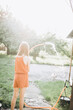 © Анна Молько - a girl in an orange overall plays with a dog in the garden, watering with water from a hose. backlight summer photo