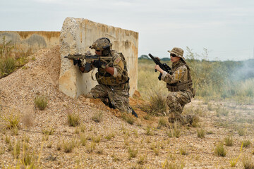 group of military soldier team in uniform with armforce training  in battle field hide behind bunker firing machine gun 
