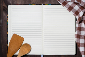 open notebook for writing recipes and kitchen spoons, top view