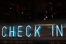 A Light Blue-colored Neon Sign Saying 'check In' On A Dark Background. A Stylish Abstract Scene, For Presentation Background Or Advertisement Purposes For Hotels Or Conferences.