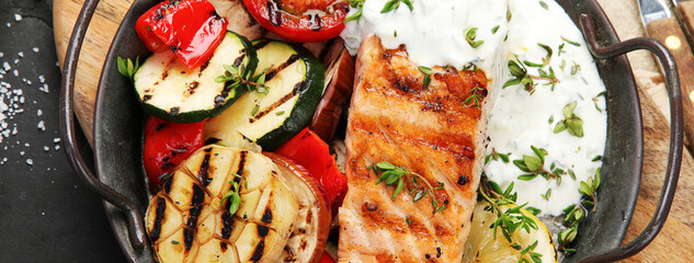 Canvas Print - Salmon steak with vegetables and white sauce on dark background.