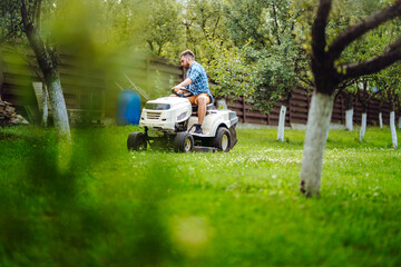 Wall Mural - Professional gardener and lawn mower cuts the grass using tractor. Industrial landscaping works