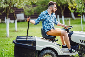 Wall Mural - Portrait of gardener using a lawn mowing tractor for cutting grass. professional gardening details