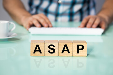 Office worker at a computer, wooden blocks, ASAP abbreviation, As soon as possible, Corporate phrase used in marketing and business