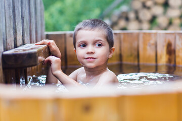  cute little boy is sweeming in big wooden furaco bath.boy baths