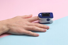 Hand finger with a pulse oximeter on a blue-pink pastel background. Measure the saturation of hemoglobin with oxygen in arterial capillary blood.