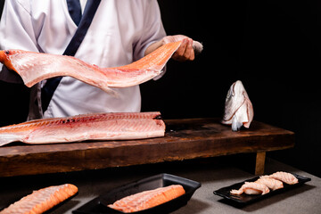 Chef's hand holding fresh piece of salmon.Closeup of chef hands preparing japanese food. Japanese chef making sushi at restaurant.Chef making traditional japanese sushi on wood board.