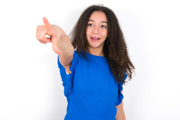 Wall Mural - Teenager girl with afro hairstyle wearing blue T-shirt over white wall  Pointing with finger surprised ahead, open mouth amazed expression, something on the front.