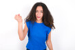 © Roquillo - Teenager girl with afro hairstyle wearing blue T-shirt over white wall  angry and mad raising fist frustrated and furious while shouting with anger. Rage and aggressive concept.