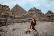 Young redhead tourist girl in brown dress sitting on a stone in Egypt, Cairo - Giza. Pyramids on backround. Copy space