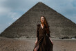 Young redhead tourist girl wearing a brown dress standing on the sand in Egypt, Cairo - Giza. Pyramid of Cheops on backround. Copy space