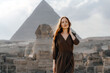 Young redhead woman standing in front of the Great Sphinx of Giza with the amazing Pyramid at the back. Valley of the Kings, Cairo, Egypt.
